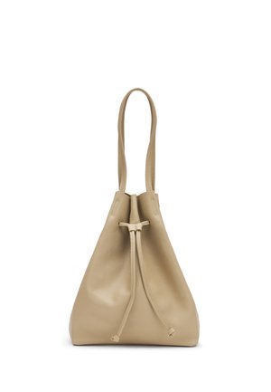 Sac bourse en cuir beige avec fermeture à cordon et longue bandoulière, posé debout sur fond blanc.