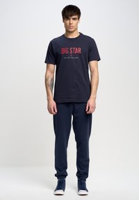 Camiseta de algodón azul marino con "BIG STAR" impreso en rojo, combinada con pantalones de chándal azul marino a juego y zapatillas de caña alta azules.