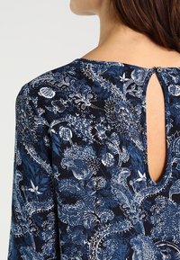 Marinebluse mit floralem Muster, Rundhals-Ausschnitt, sowie einem Schlitz mit Knopfverschluss im Rücken. Weicher Stoff mit filigranen blau-weißen Mustern.