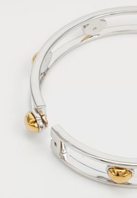 Bracciale rigido in argento con tre accenti a forma di cuore in oro, design elegante e finitura liscia con una texture lucida e uno stile minimalista.