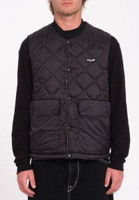 Chaleco negro acolchado con cuello de canalé, que cuenta con dos bolsillos delanteros y un pequeño logo en el pecho. Textura lisa con cierre de botones a presión.