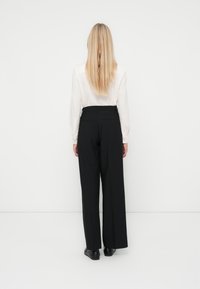 Black wide-leg trousers with a high waist, smooth fabric, rear pockets, and a clean silhouette, paired with a light-colored shirt.