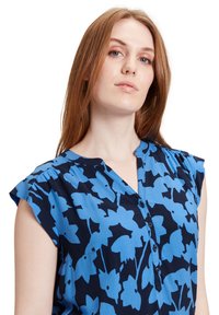 Blå bluse med blomsterprint, rund halsudskæring, knaplukning front og cap sleeves. Lavet af letvægtsstof med en glat tekstur.