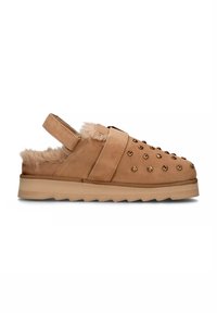 Scarpa slip-on in suede tan con fodera in pelliccia, dettagli borchiati e suola in gomma spessa. Presenta una cinghia posteriore per una vestibilità sicura.