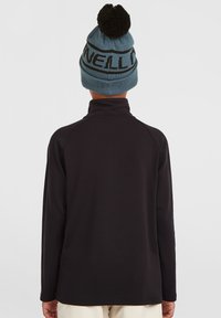 Langsleeve zwart top met een hoge kraag, gecombineerd met een blauwe gebreide beanie met een zwarte band en pompon-detail bovenop.