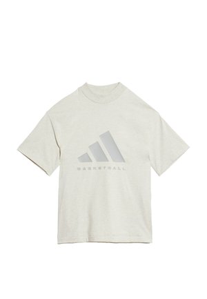 Person iført lysebeige oversized Adidas T-shirt og matchende shorts med Adidas Basketball-logo på brystet.