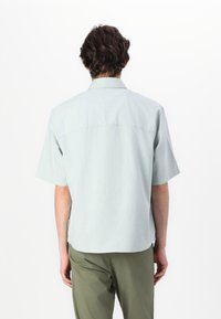 Chemise à manches courtes, vert clair, en tissu doux, dotée d'un col classique et d'un ourlet droit avec un design simple.