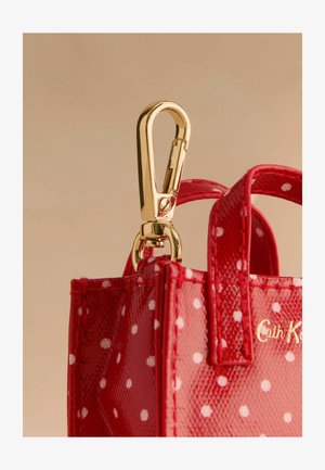 Rote Lackleder-Handtasche mit weißen Punkten, ausgestattet mit goldenen Clips und kleinen Griffen zum Tragen oder Befestigen.