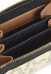 Monedero texturizado que combina tela negra y cuero beige, con cierre de cremallera dorada, múltiples compartimentos y fondo tejido en color crema.