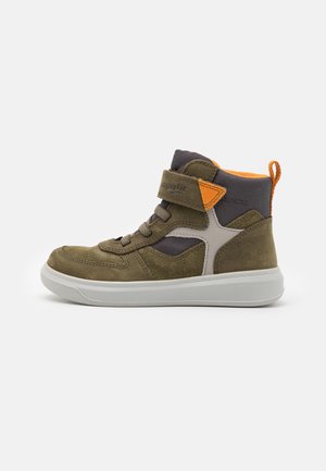 Hoge sneaker in olijfgroen met witte zool, oranje trekkoord, grijze stof aan de enkelkraag, veters en een klittenbandsluiting op een lichte achtergrond.