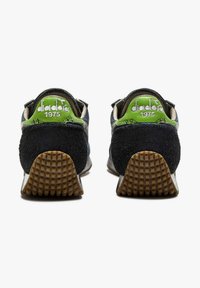 Baskets en suède vert et noir avec une semelle en caoutchouc texturé. L'arrière présente des logos blancs et verts : "diadora" et "1975."