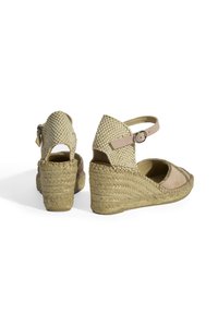 Sandales à semelle en jute, tige en daim beige et talon tissé. Bride de cheville réglable avec une petite boucle métallique.