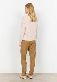 Hellrosa Langarmoberteil, bequeme beigen Hosen und Schuhe in hellen Farbtönen. Glatte Textur, minimalistisches Design und neutrale Farben.