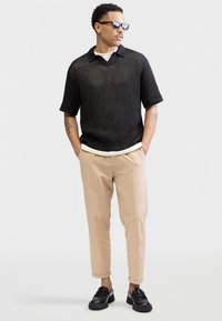 Mustast lõngast lühikeste varrukatega polo särk valge sisesämblusega, kombineeritud beežide kitsenevate pükstega ja mustade libisevate jalanõudega.