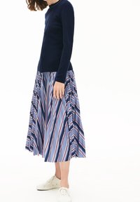 Marinblå långärmad topp kombinerad med en plisserad, randig kjol i ljusblått, rött och marinblått. Vita sneakers fulländar outfiten.