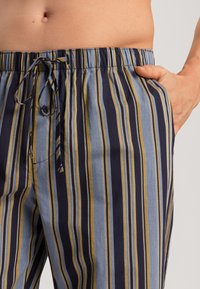 Gestreepte katoenen broek met een trekkoord in de taille. Kleuren zijn marineblauw, lichtblauw en goud. Heeft een zijzak en een zachte textuur.