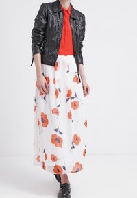 Schwarze Lederjacke mit Reißverschlusstaschen, rotem Oberteil und einem weißen Maxikleid mit floralen Mustern in Orange und Marineblau. Schwarze Schuhe.