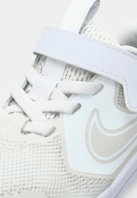 Nike sneakers met een lichtgrijze mesh bovenkant, witte lederen accenten, gestructureerde veters en een klittenbandsluiting over de middenvoet.