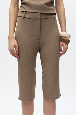 Personne portant un pantalon court taille haute taupe et un haut assorti, avec deux bracelets épais au poignet droit.