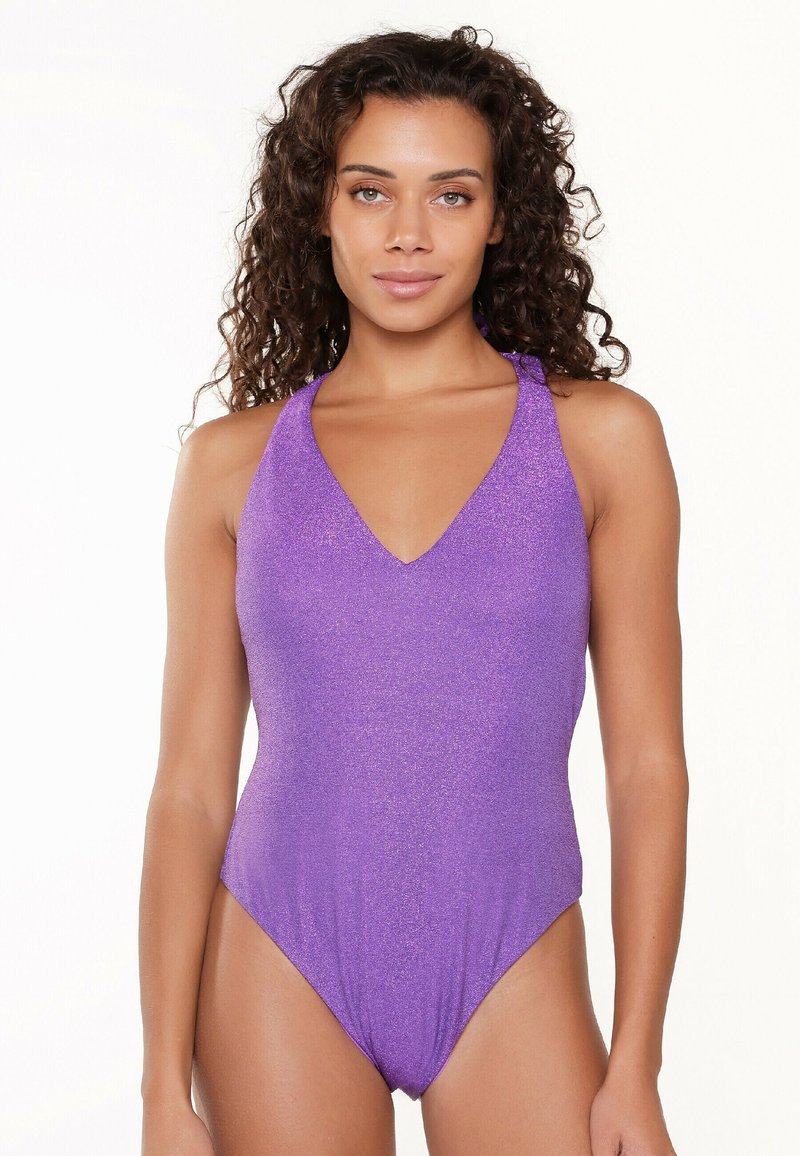 Maillot de bain une pièce violet avec un décolleté en V, des bretelles à nouer autour du cou et une texture brillante. Les jambes hautes soulignent la silhouette. Sans motifs ni détails en métal.