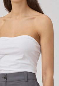 Top blanc sans bretelles, design ajusté avec une texture lisse, associé à un pantalon gris taille haute avec un détail de bouton.