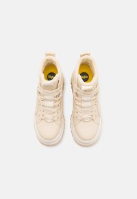 Beige høy-top sneakers med en teksturert stoffoverdel, hvite snørebånd, en polstret kant og en gul innersåle med logodetalj.