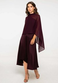 Conjunto de dos piezas burdeos con un top de capa transparente y falda fluida. Textura suave, corte holgado, con tacones de pulsera en un acabado metálico.