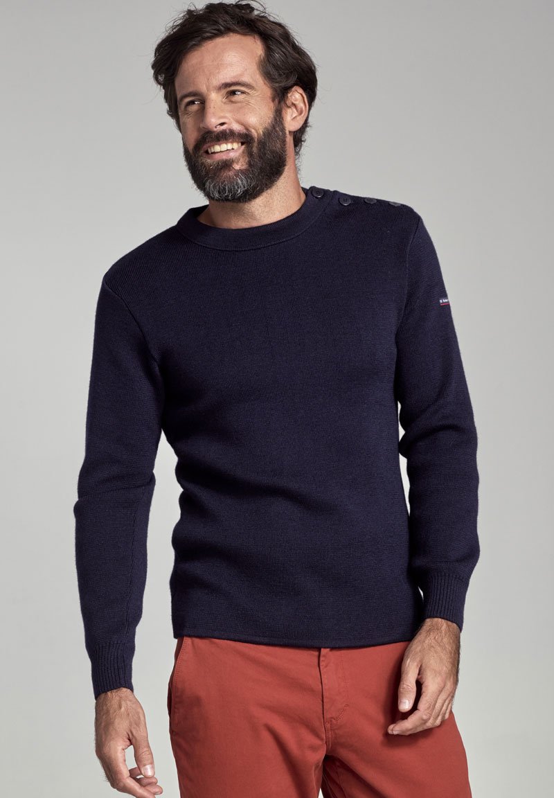 Pull en maille bleu marine avec un col rond et des boutons aux épaules. Présentant des poignets et un ourlet côtes. Assorti à un pantalon rouge.