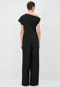 Top nero off-shoulder con maniche corte, realizzato in tessuto liscio. Abbinato a pantaloni neri a gamba larga, che offrono una silhouette sartoriale.