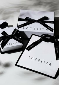 Tre scatole regalo bianche con nastri neri, decorate con il logo "LATELITA" in nero sulla parte frontale, di diverse dimensioni e forme.