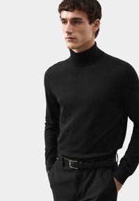 Černý rolák vyrobený z měkkého materiálu, přiléhavý střih, dlouhé rukávy, nošený s elegantními kalhotami a černým opaskem.