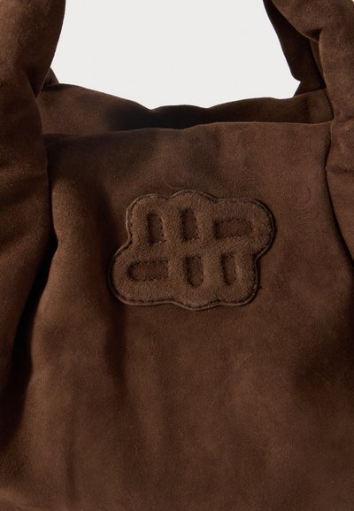 Pruunist sametist kott, millel on tekstureeritud viimistlus. Omandab silmapaistva pruuni logotähise lõikega detailidega. Pehme ja paindlik kuju.