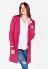 Cardigan lungo fucsia con due tasche frontali, apertura anteriore e polsini a righe bianche, indossato sopra una maglietta bianca e jeans blu. Texture liscia.