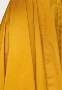 Żółta kurtka wykonana z gładkiego, lekkiego materiału, z pionowymi plisami, starannym szyciem i teksturowanym wykończeniem.