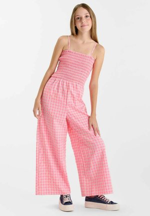 Tuta intera a quadretti rosa e bianca con corpetto arricciato, pantaloni ampi e spalline sottili. Abbinata a sneaker blu navy con suole bianche.