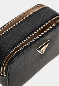 Borsa a tracolla in pelle nera texture con due zip dorate visibili e un piccolo logo triangolare dorato.