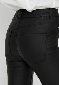 Jeans noirs slim adaptés avec une texture lisse, des poches arrière avec des détails cousus, et une taille haute pour un ajustement confortable.