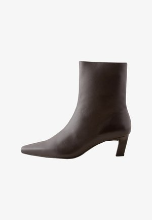 Brūnas ādas potītes zābaki ar norādītu purngali un īsu, kvadrātveida papēdi. Gluda tekstūra, minimālisma dizains, nav redzamu rakstu vai rotājumu.