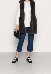 Grå faux päls lång väst över en vit skjorta med knappar, i kombination med avklippt blå denim och svart-vita loafers. Svart kviltad handväska.