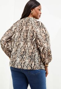 Bluse med lange ærmer, der har et beige og brunt slangeskindsprint, tekstureret stof, samlet halsudskæring og let puffede ærmer. Stylet med mørke jeans.