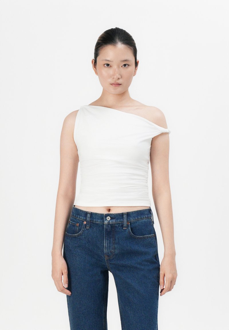 Hvitt én-skulder topp med rynket design, paret med blå høyt liv denimjeans med knappelukking og fem-lommestil.