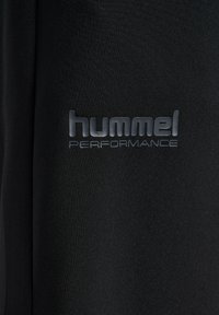 Zwarte sportkleding van stof met een glanzend "hummel PERFORMANCE"-logo, met een gladde textuur en minimalistisch ontwerp.