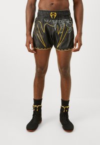 Black boxing shorts with yellow accents and a patterned design on the side. Features an elastic waistband and a logo patch.