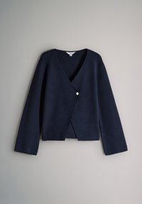 Cardigan en maille bleu marine à manches longues, col en V profond et une seule fermeture par bouton décentré sur un fond gris clair.