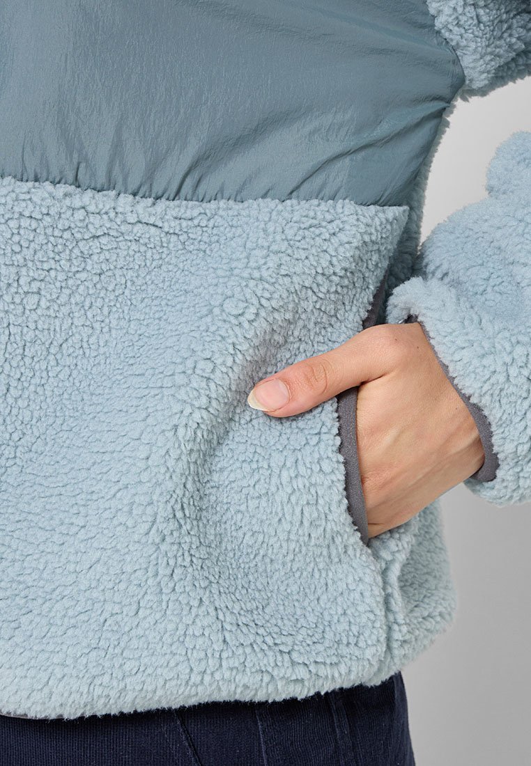 Fleece-Pullover in Hellblau, mit einem weichen, strukturierten Unterteil, glattem oberen Teil und seitlichen Taschen mit grauer Einfassung.