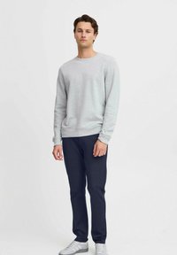 Suéter de algodón gris claro con cuello redondo, puños acanalados y dobladillo, combinado con pantalones azul marino y zapatillas deportivas blancas.