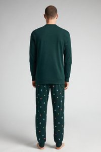Top de algodón verde de manga larga con escote redondeado, combinado con pantalones de pijama estampados que presentan motivos coloridos sobre un fondo verde oscuro.