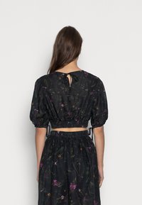 Crop top nero con motivo floreale, maniche a sbuffo, vita arricciata e chiusura con fiocco sul retro. Presenta piccoli motivi di fiori colorati su tutta la superficie.