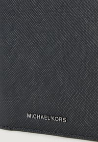 Granatowy, teksturowany portfel skórzany z diagonalnym wzorem i srebrnym logo "MICHAEL KORS" w prawym dolnym rogu.