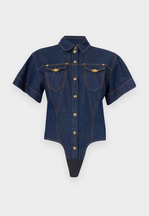 Teloový overal z tmavého denimu s krátkym rukávom, zlatými gombíkmi, prednými náprsníkovými vreckami s klopou a kontrastným oranžovým prešitím na svetlom pozadí.